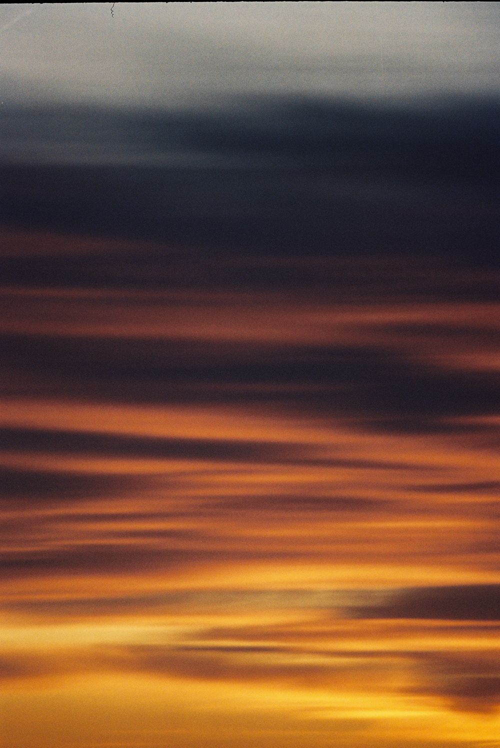 Dramatic sunset sky with vibrant orange and golden clouds layered beneath dark storm clouds at dusk.