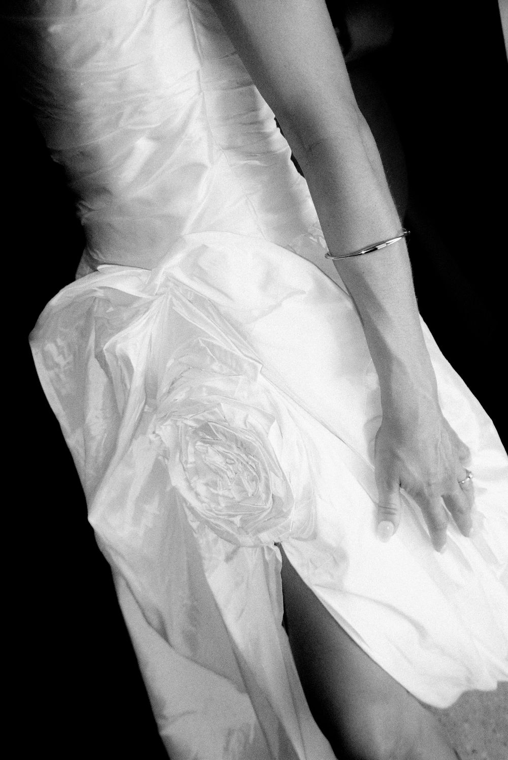 Close-up of a bride in a white wedding gown with a floral detail, wearing a delicate bracelet and ring.