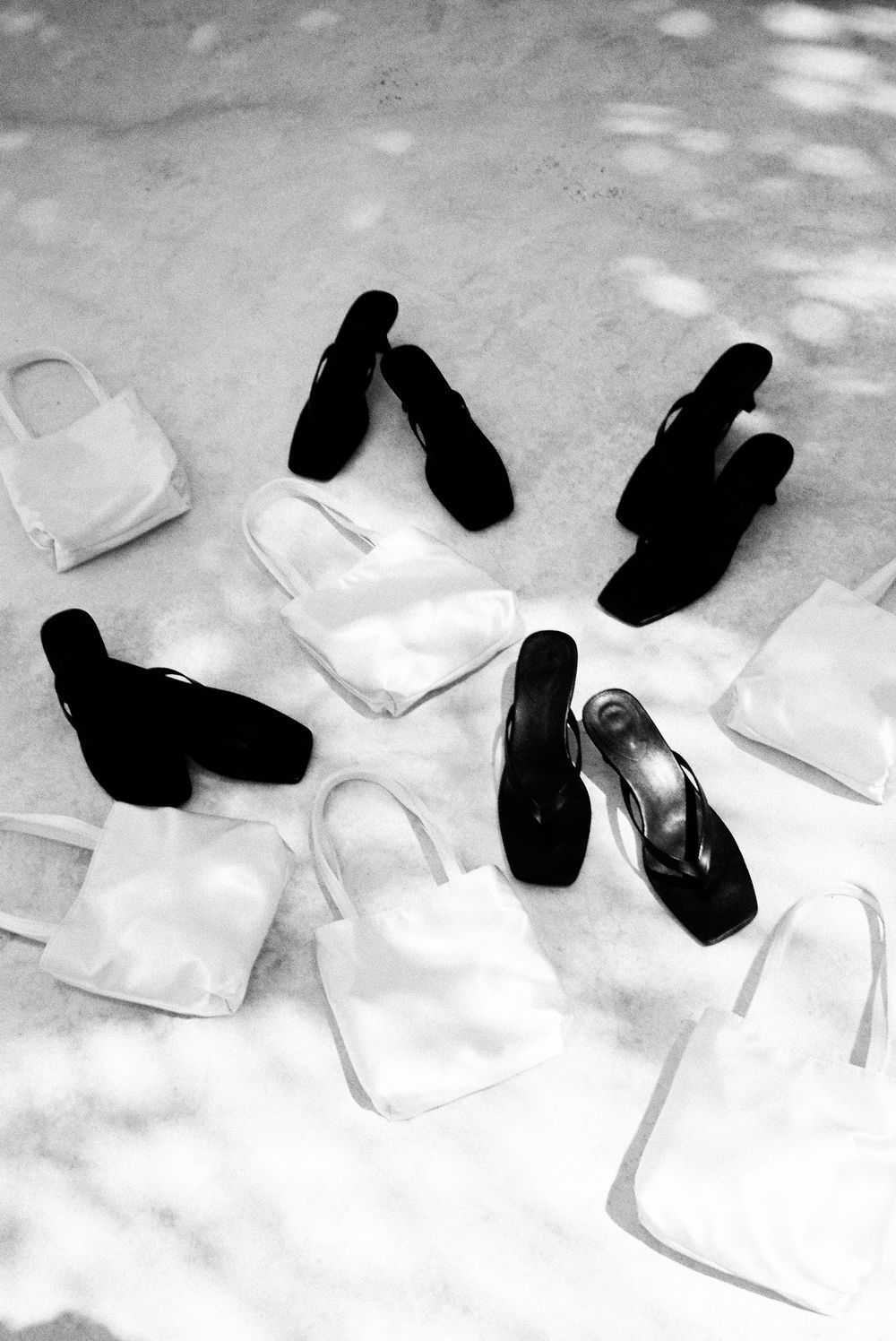 Black and white photo of sandals and tote bags arranged on ground.