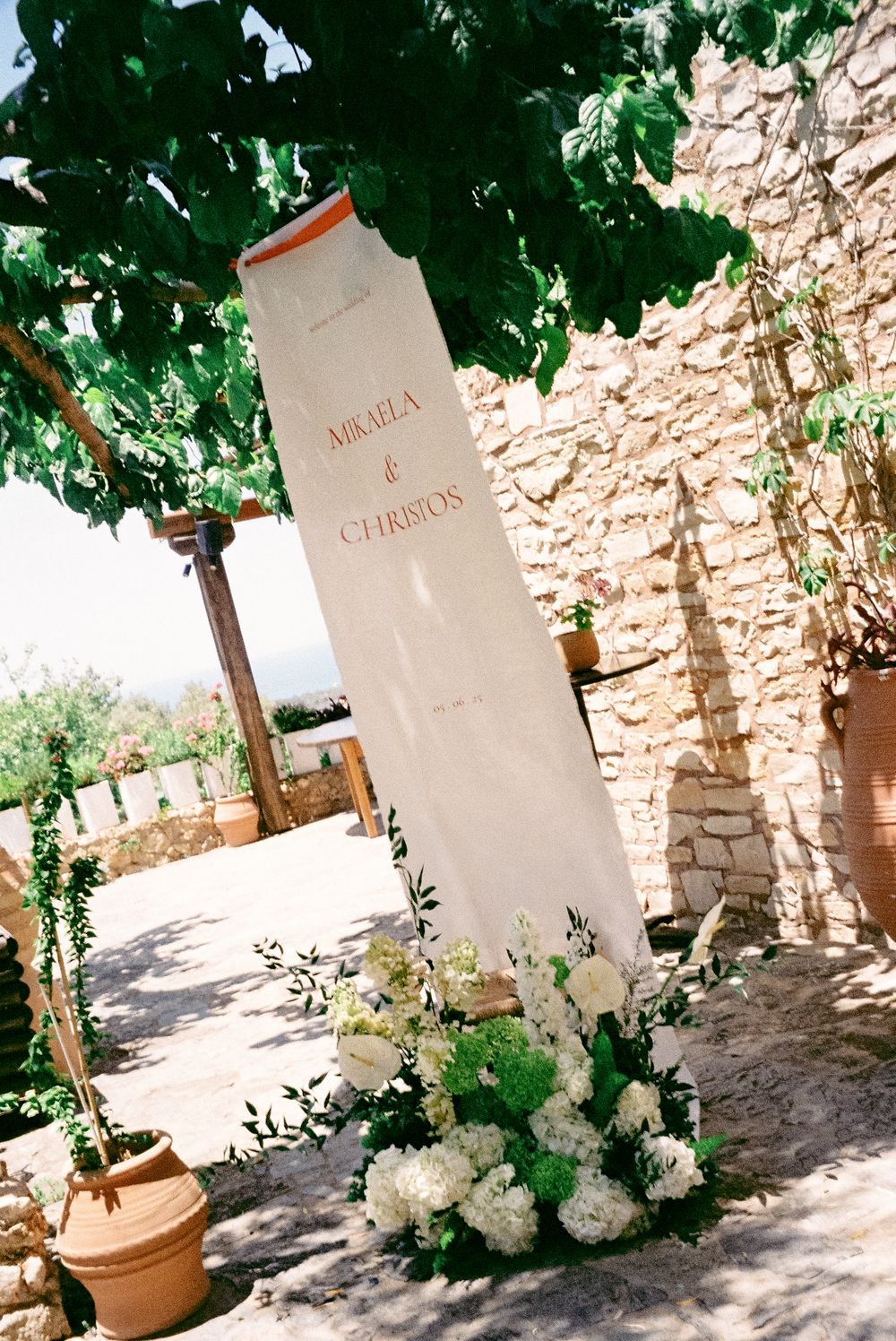Elegant wedding welcome sign reading Mikaela and Christos adorned with white floral arrangements.
