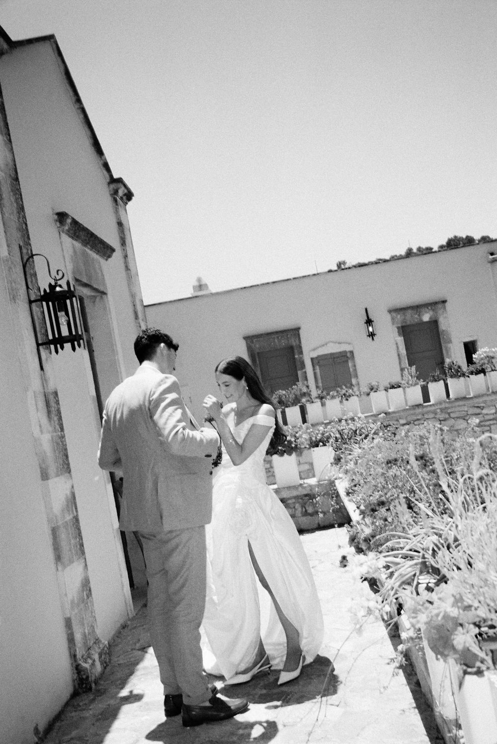 Black and white photo of a bride and groom dancing outdoors near a white building on their wedding day.