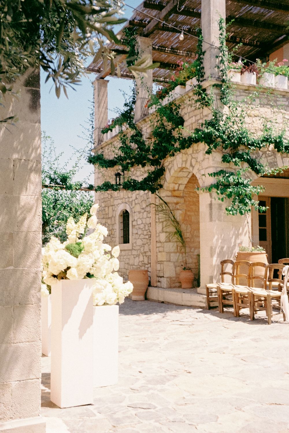 Elegant stone villa courtyard with white hydrangea floral arrangement and wooden chairs for an outdoor wedding ceremony.