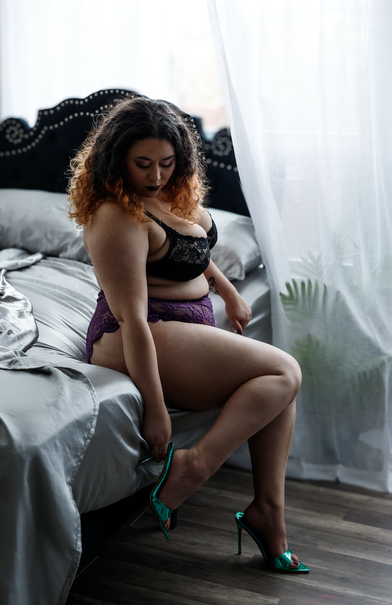 Woman in black bralette touching her neck, showcasing a delicate ring on her finger with soft natural lighting.