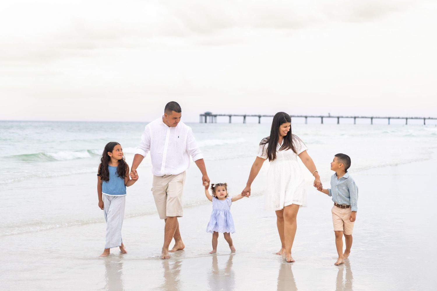Large extended family group portrait smiling together on a white sandy beach with green dunes behind.