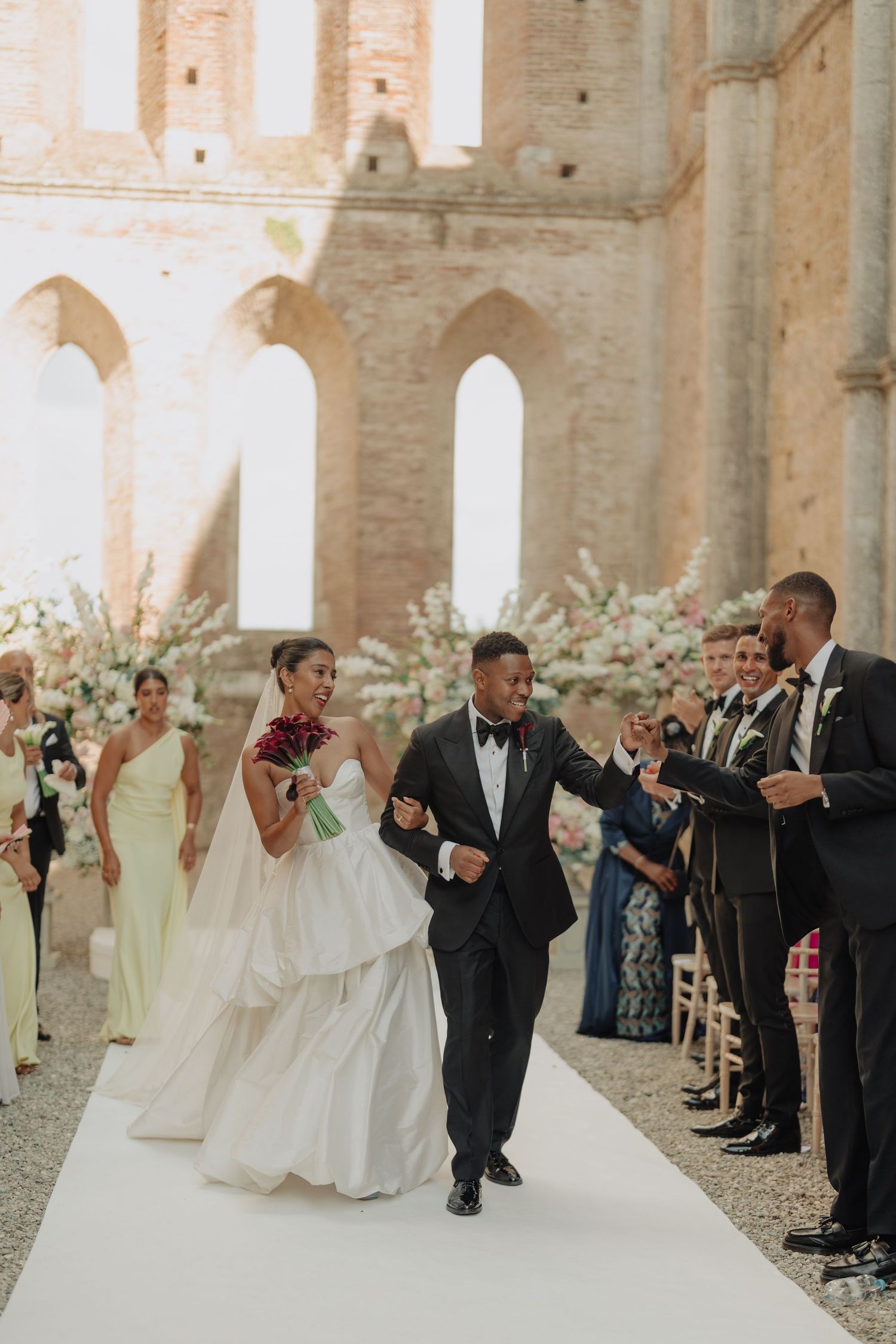 Elegant couple in wedding attire, bride in white gown and groom in black tuxedo with bow tie, posing together.