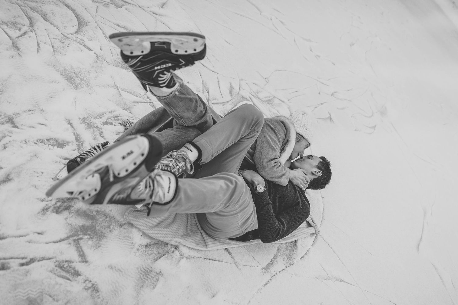 Black and white photo of a person lying on snow wearing ice skates, viewed from above.