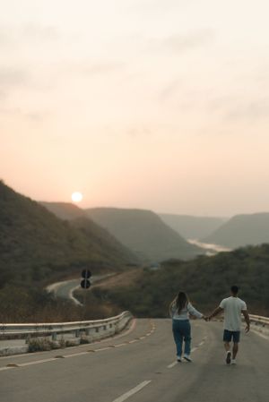 Couple walking hand in hand on winding mountain road during sunset.