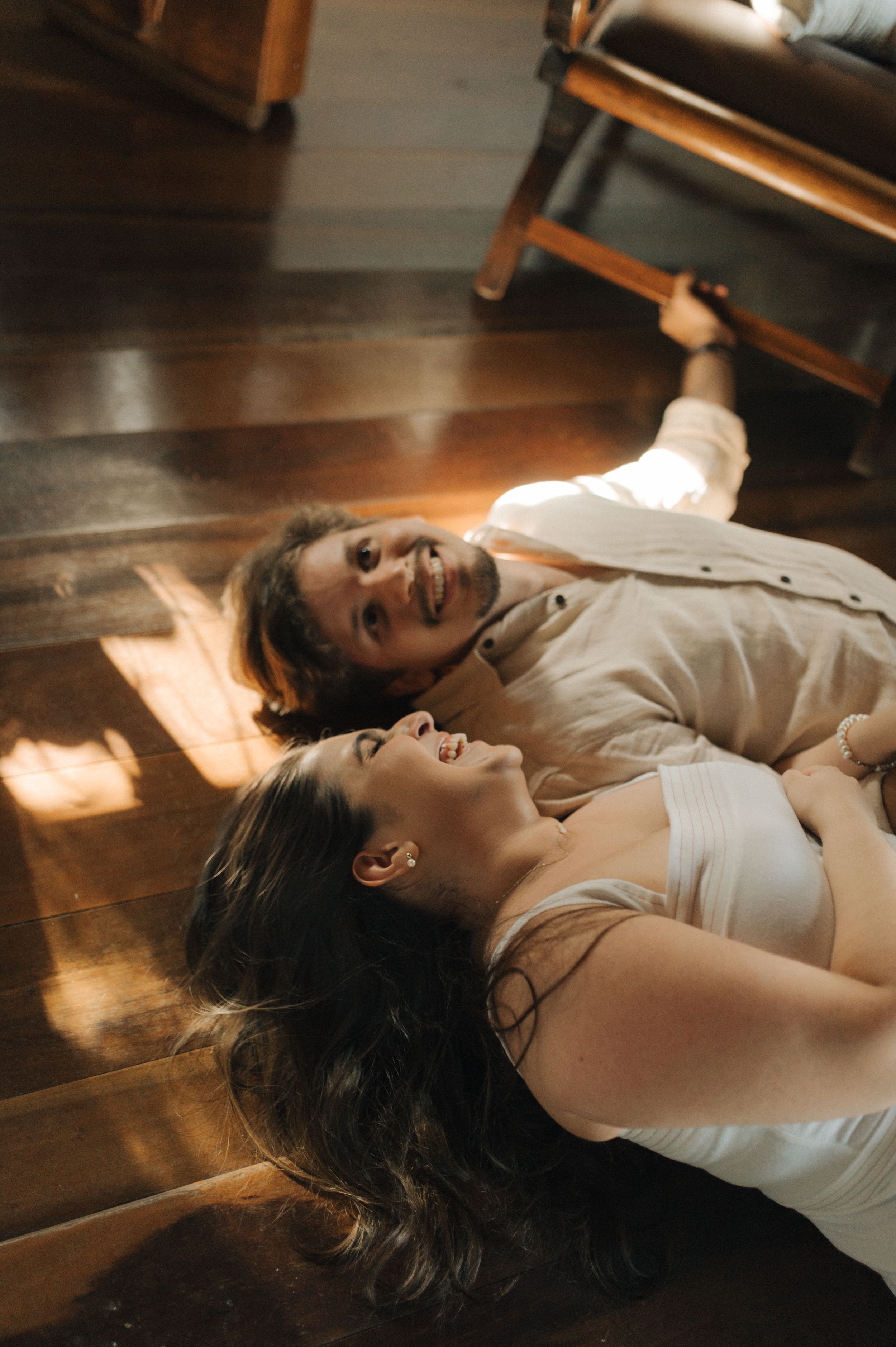Couple lying on hardwood floor in sunlight sharing a joyful moment together.