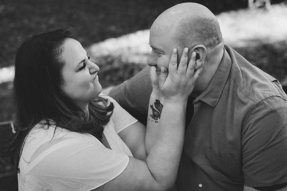 Black and white photo of a couple sharing a tender moment, woman touching mans face as they lean in for a kiss.