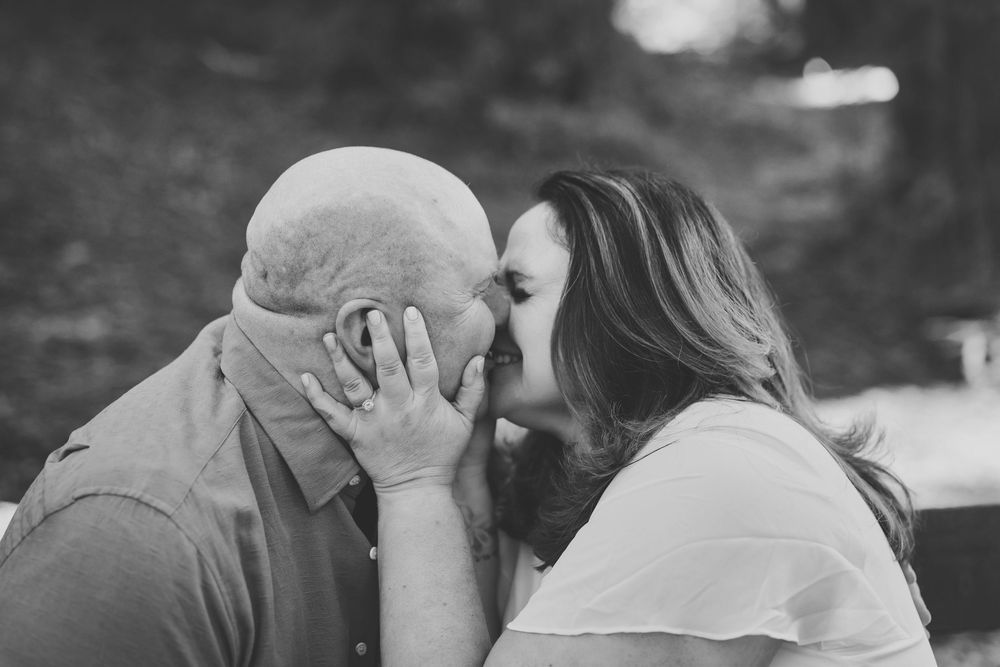 Black and white photo of a couple sharing a tender kiss outdoors, woman gently holding mans face.