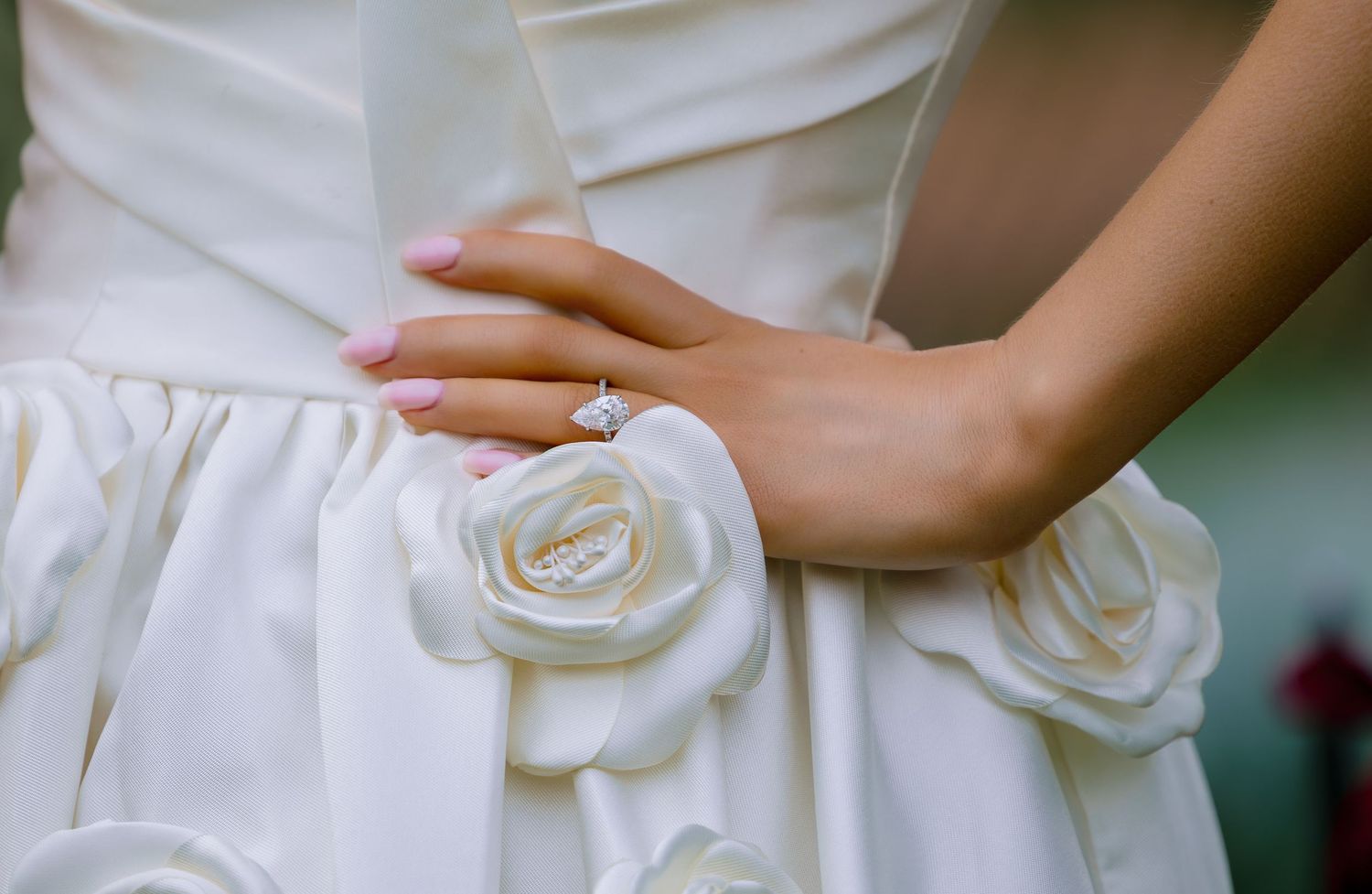 Close-up of a bride in a white satin wedding dress with rose details, wearing a diamond engagement ring.