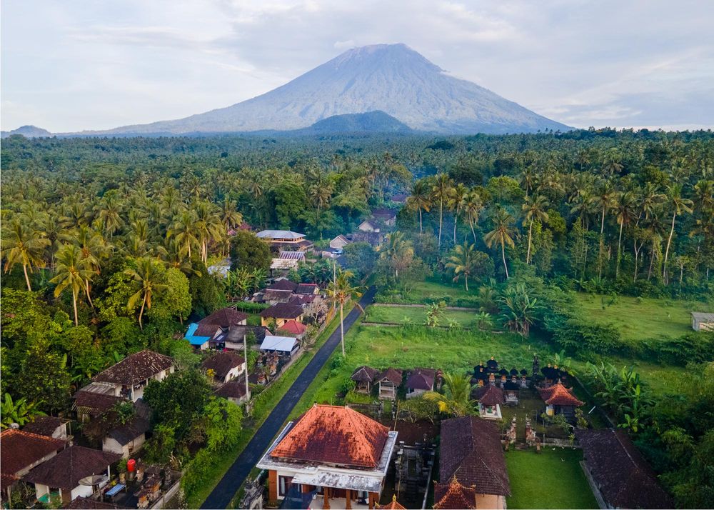 Aerial view of a lush tropical village with palm trees and a majestic volcano in the background, Bali, Indonesia.