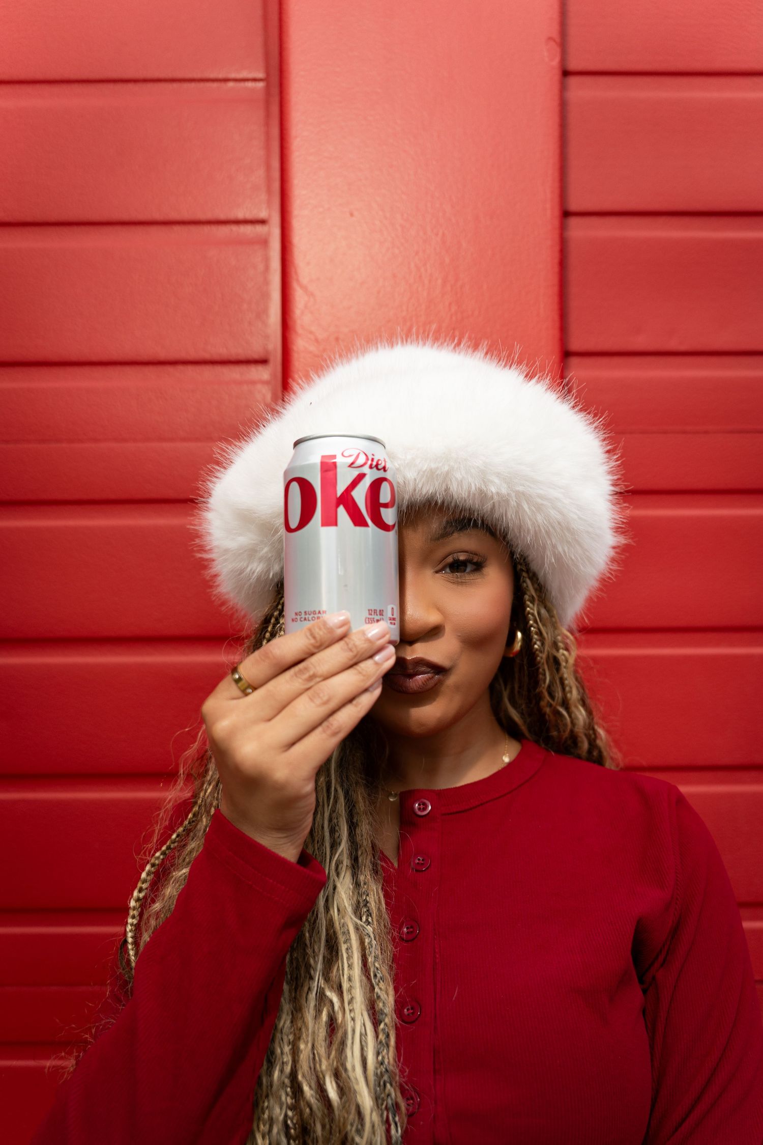 Person in red sweater and white hat against red wall background.