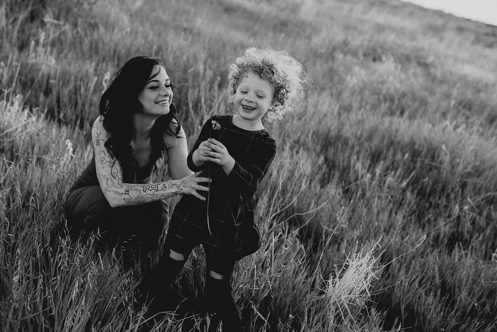 Black and white photo of a smiling woman crouching with a laughing curly-haired child in a grassy field.
