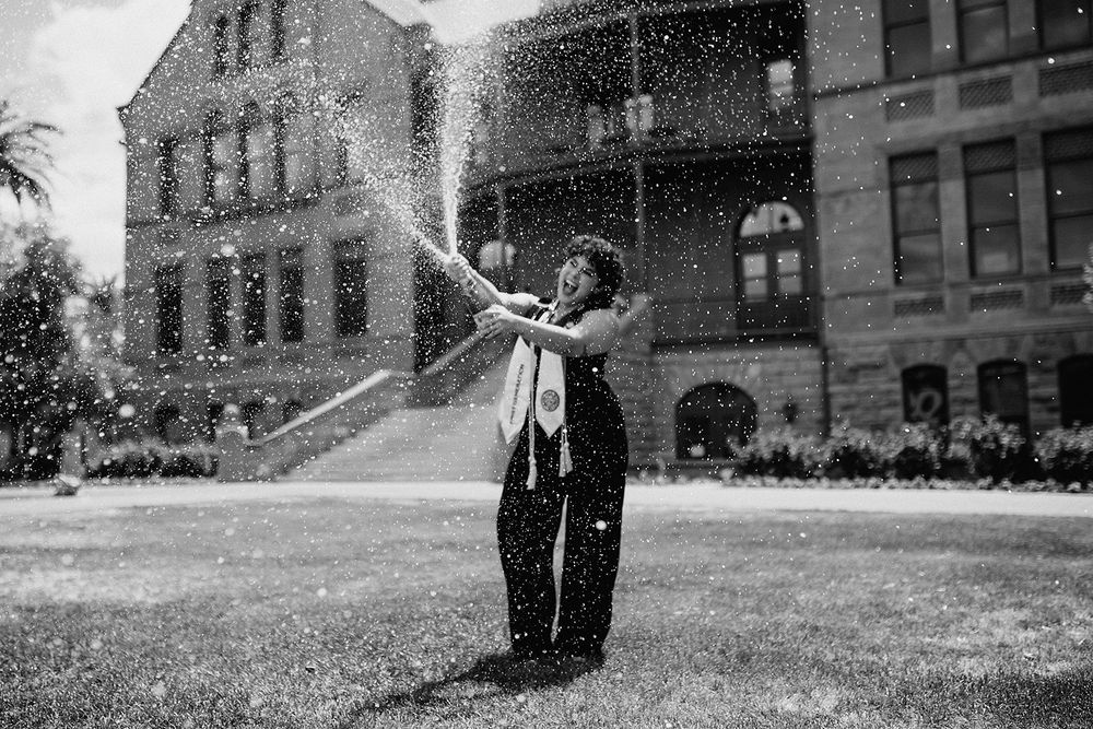 Black and white photo of a person spraying water from a hose on a lawn in front of a historic building.