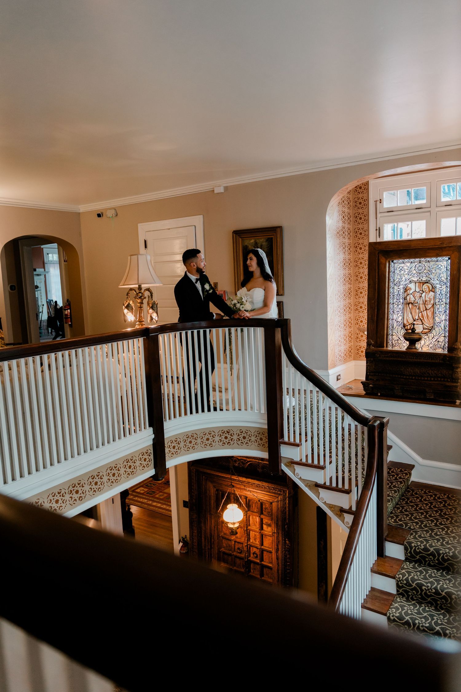 Bride and groom stand together on an elegant curved staircase landing inside a historic wedding venue.