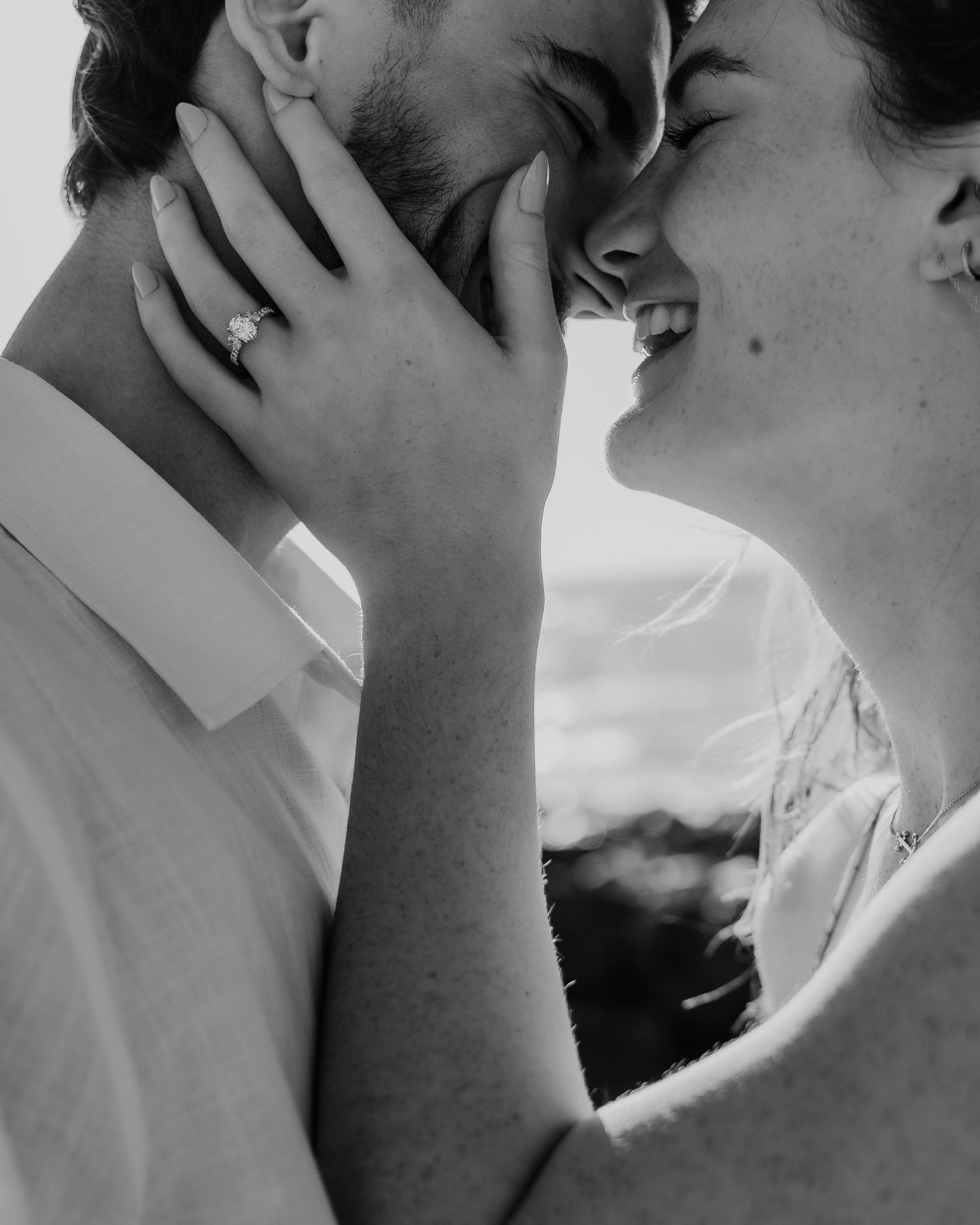 Black and white photo of a couple sharing a romantic kiss, with an engagement ring visible on the woman's hand.