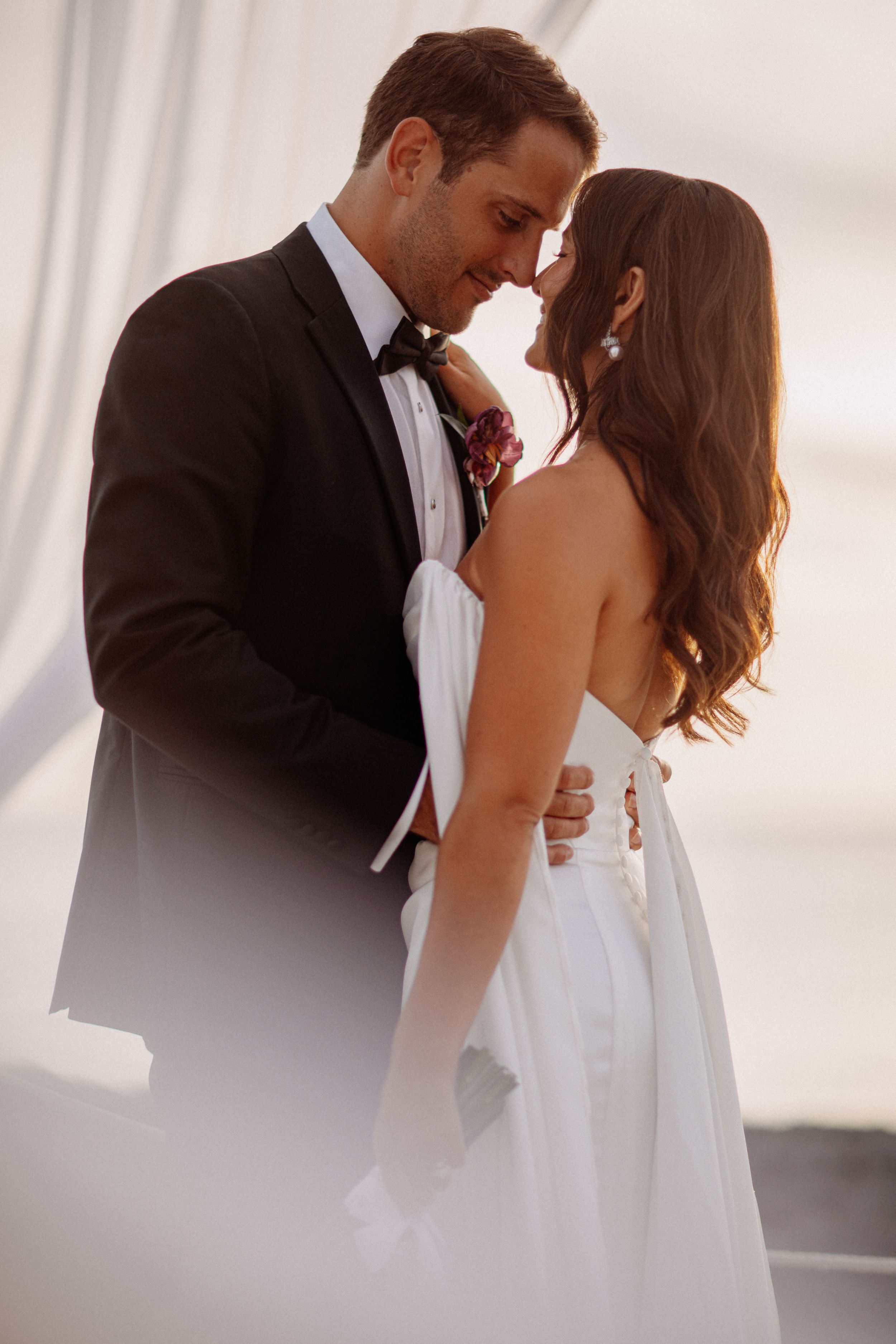A bride and groom share a romantic moment, touching foreheads, as she wears a white gown and he wears a black tuxedo.