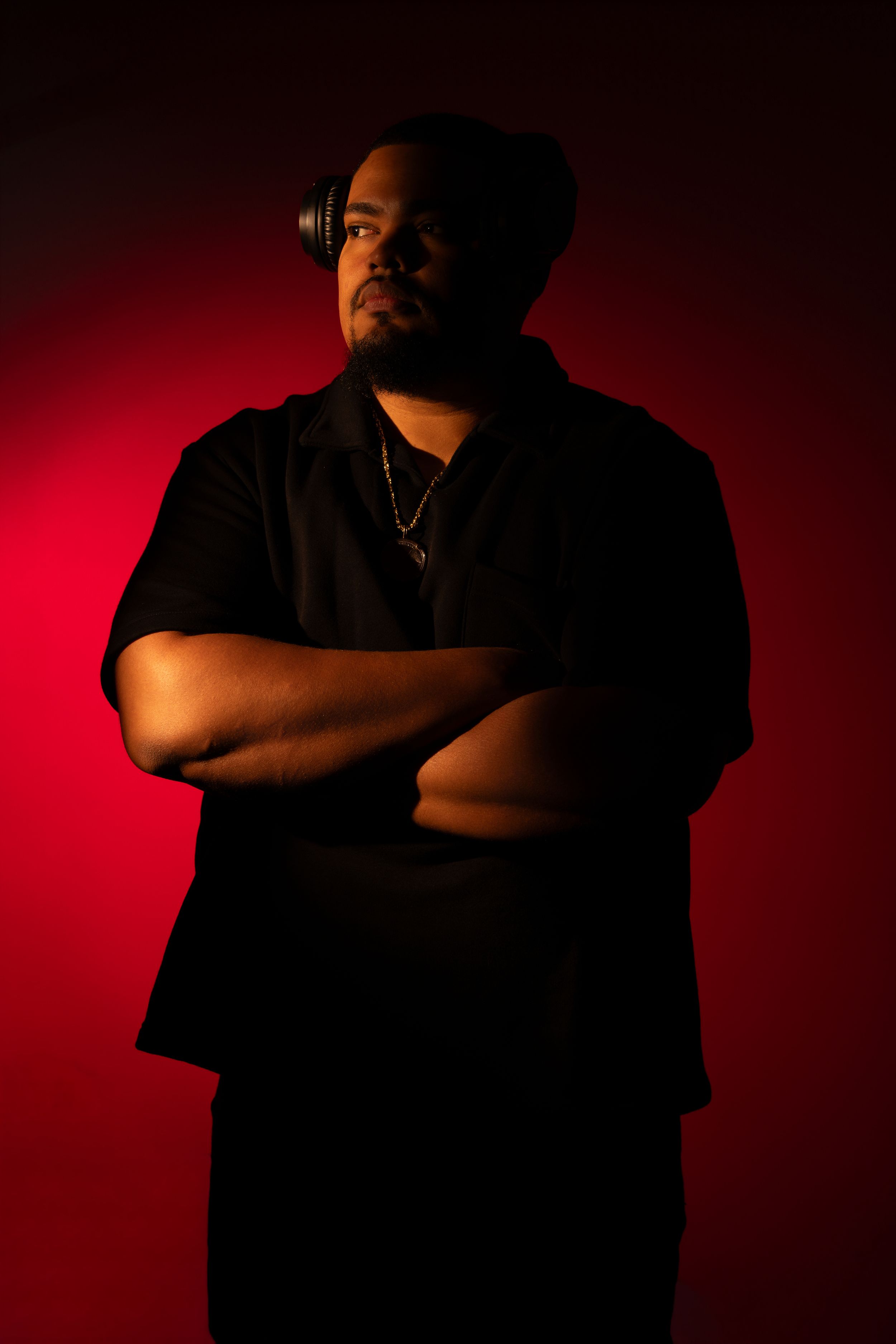 Man in black shirt with headphones poses arms crossed against dramatic red background.