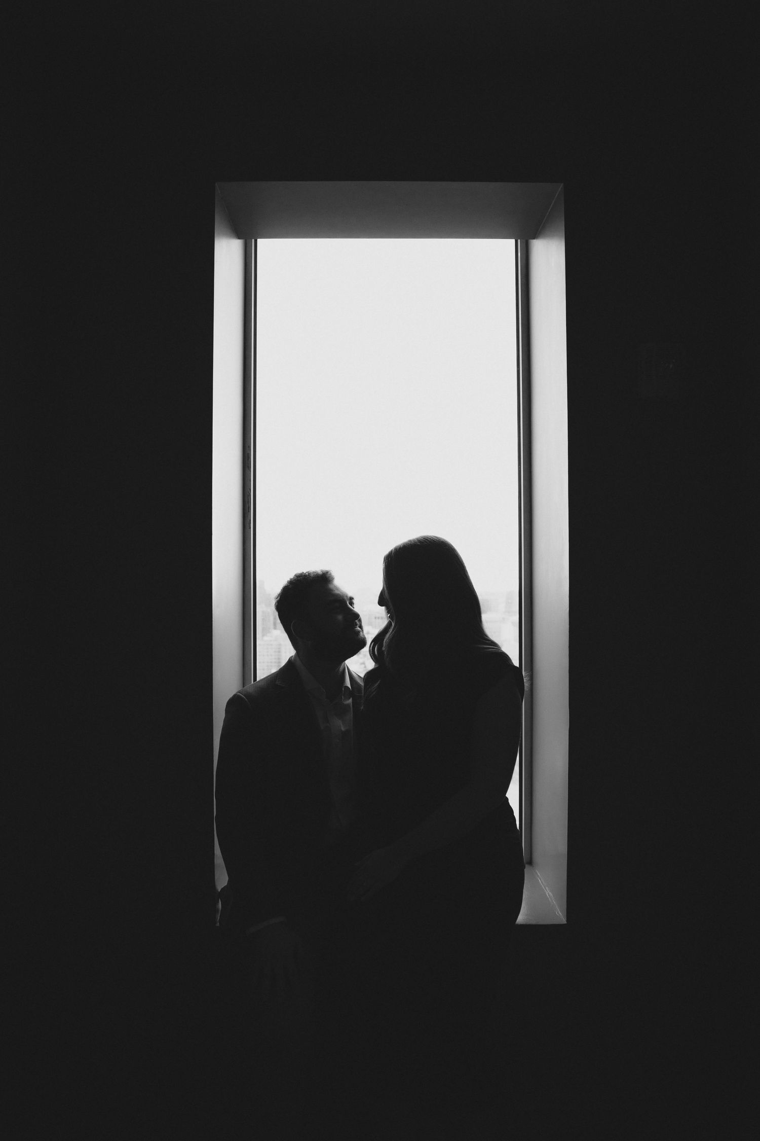 Romantic silhouette of a couple facing each other in a window, black and white photography.