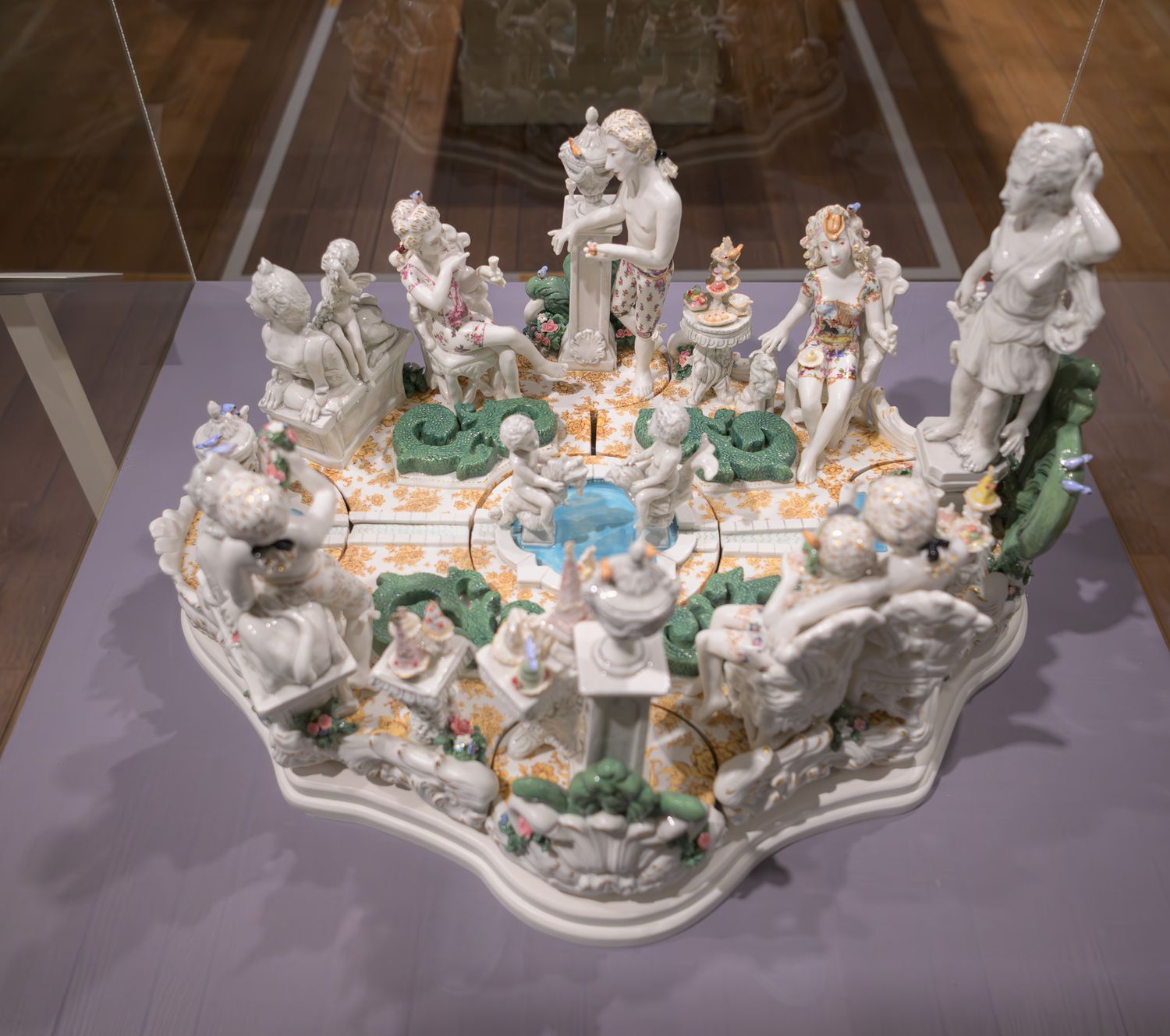 Ornate porcelain centerpiece with white figurines and colorful floral details displayed under glass in a museum.