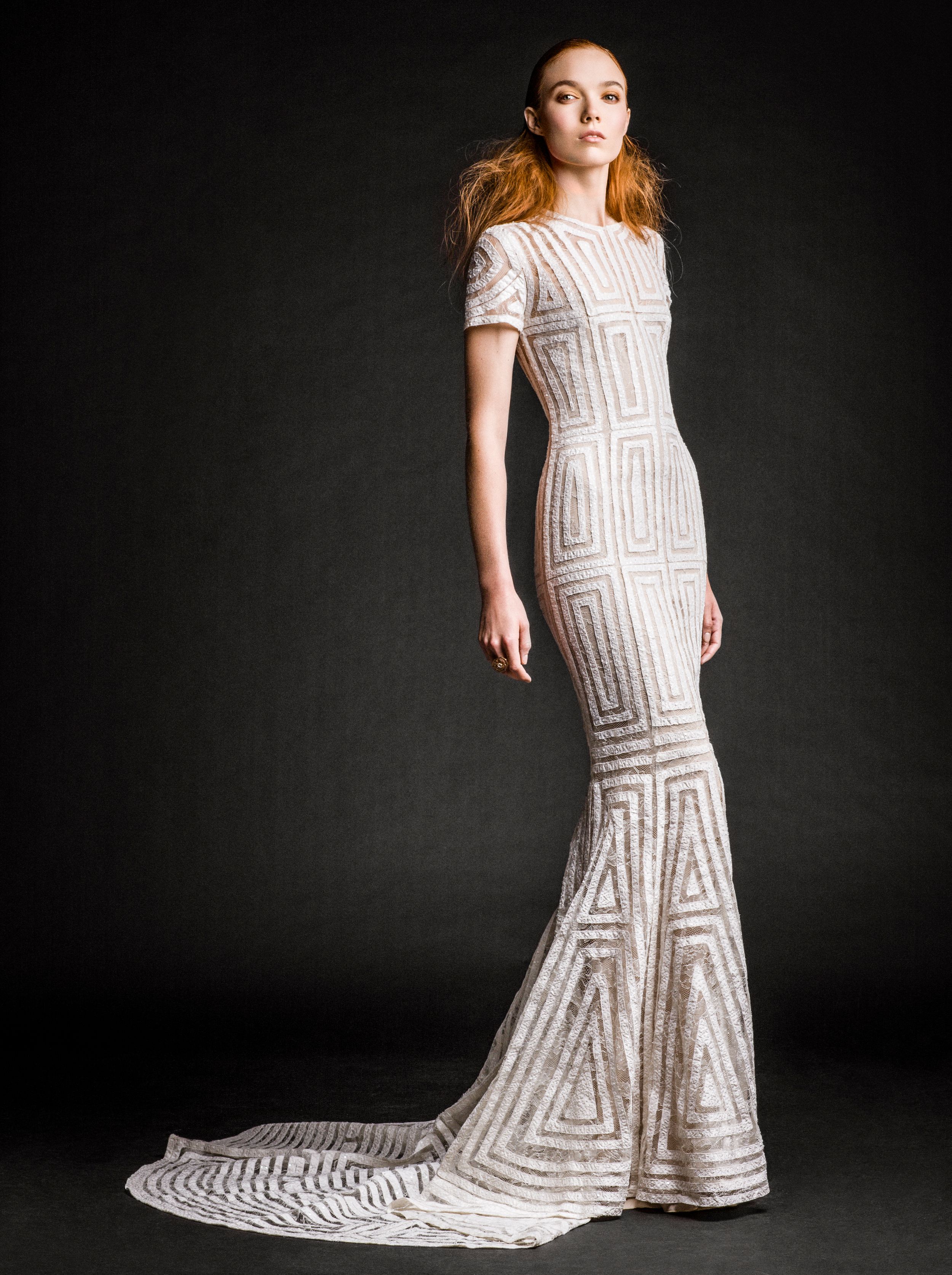 Model wearing a fitted white geometric beaded mermaid wedding gown with short sleeves and a train.