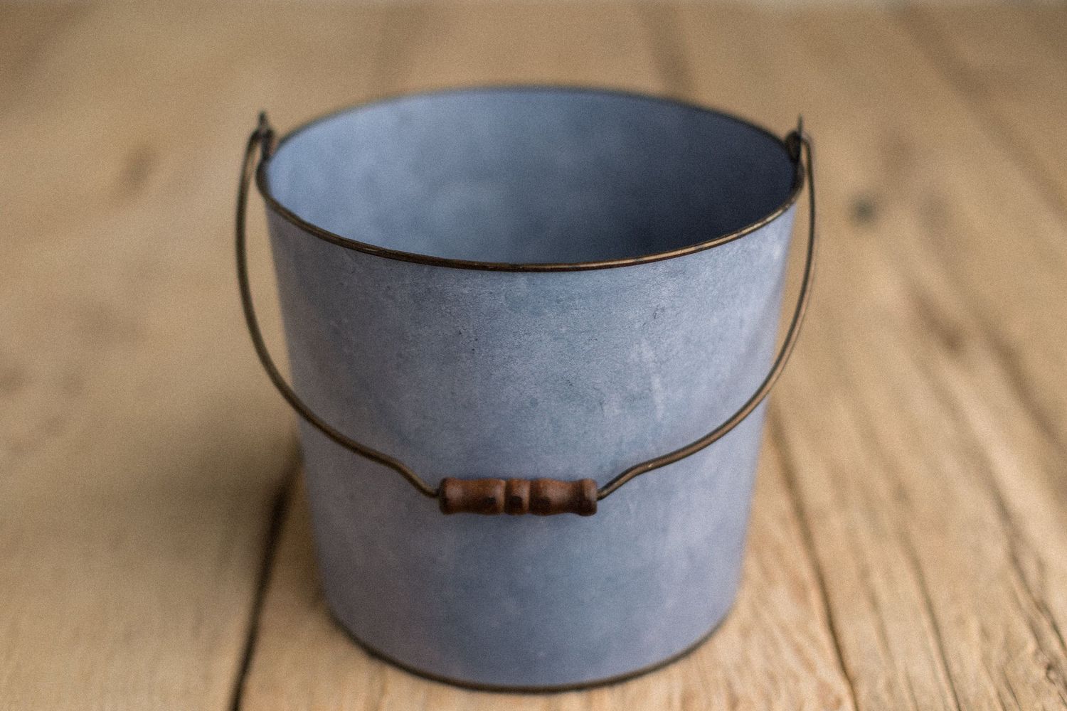 Rustic gray galvanized metal bucket with wooden handle bead, sitting on a wooden surface.