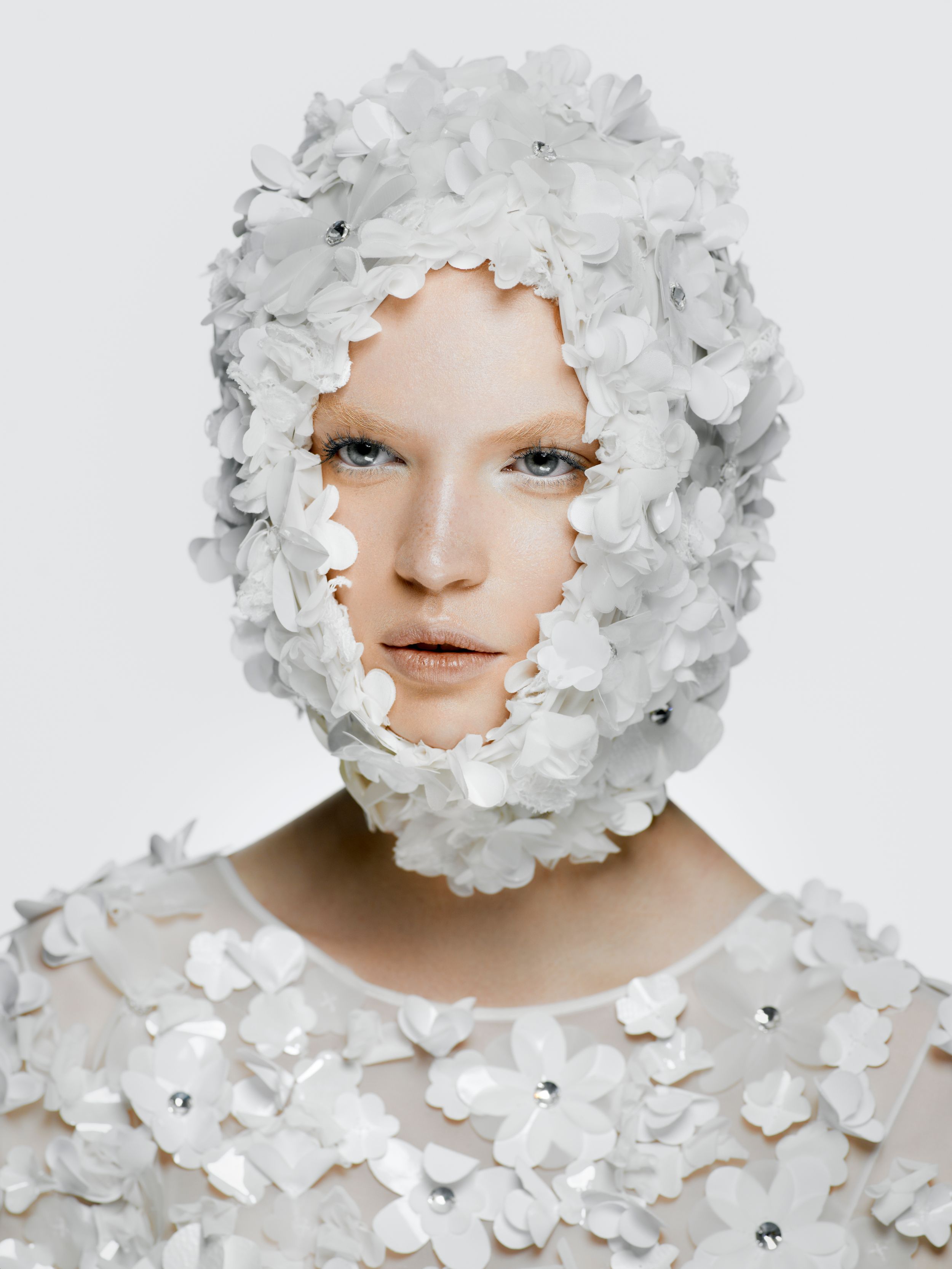 Model wearing white floral headpiece and embellished top covered in delicate white flowers and crystals.