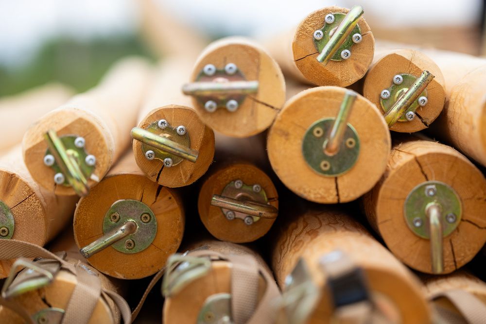 Stacked wooden logs with metal hinges and screws on cross-section ends, showing natural wood grain texture.