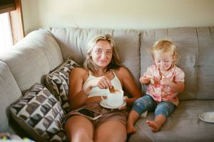 Woman and toddler sitting on gray couch sharing cake together in a cozy living room setting.
