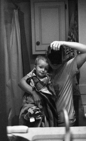 Black and white photo of a young child wrapped in a blanket held by an adult taking a mirror selfie.