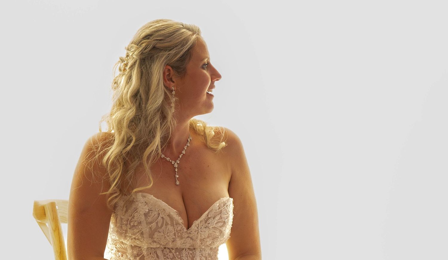 Une mariée élégante vêtue d'une robe bustier en dentelle, arborant un collier en diamants et une chevelure blonde légèrement ondulée.