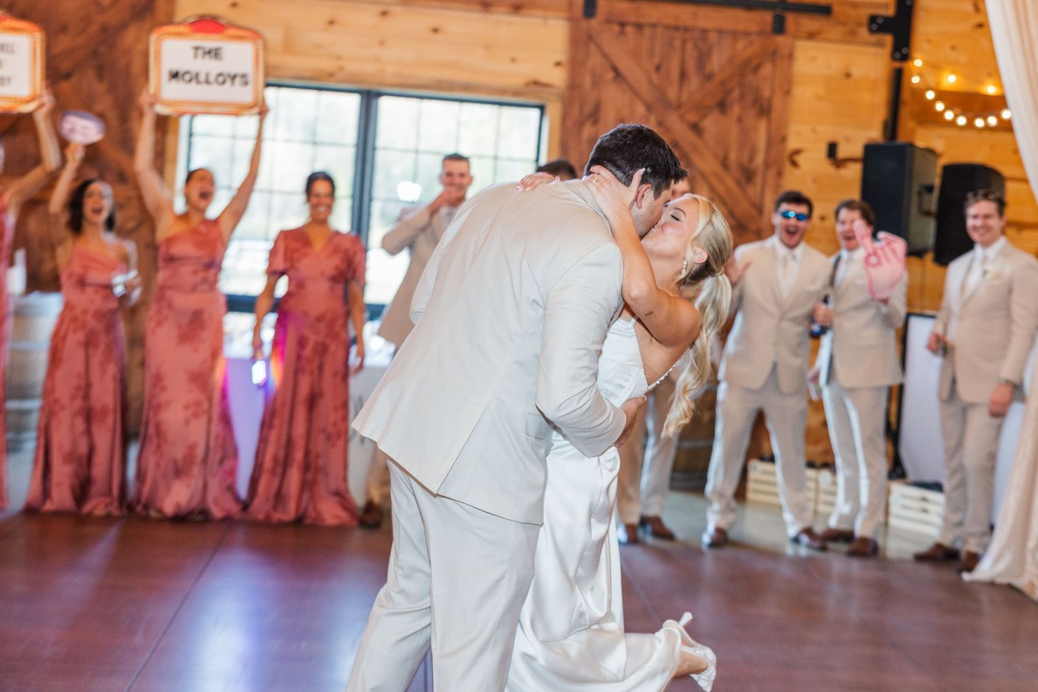 Bride and groom share a romantic dip kiss on the dance floor at a rustic barn wedding reception.