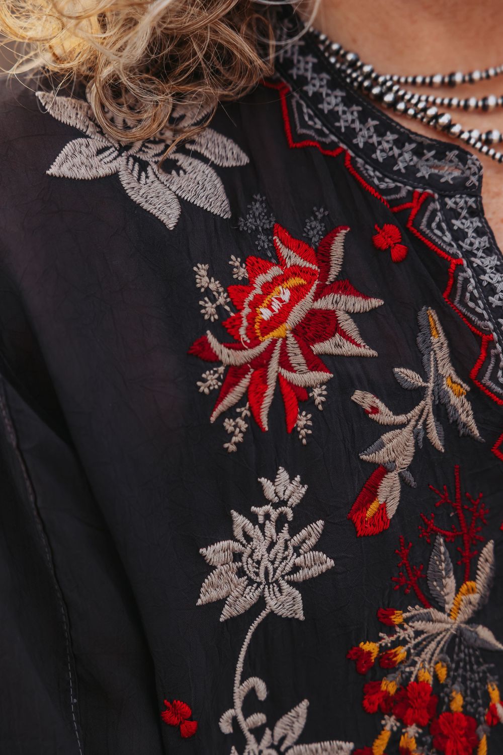 Black blouse with colorful floral embroidery featuring red, gray, and yellow flowers on chest.