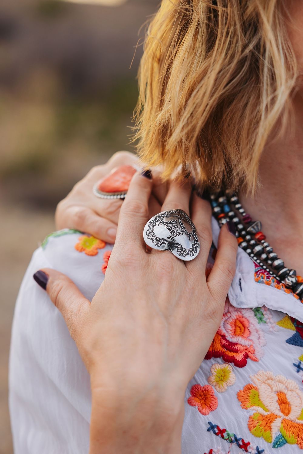 Close-up of a woman wearing a large silver tree of life ring and colorful floral embroidered top with beaded necklace.