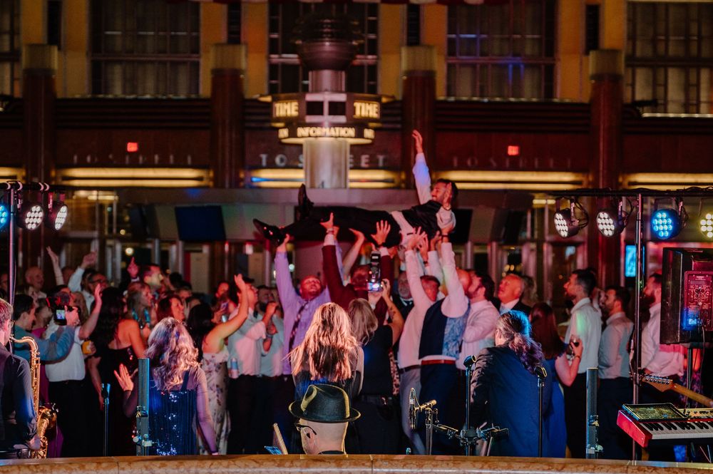 Crowd of party guests dancing and celebrating at an outdoor evening event with colorful stage lighting.