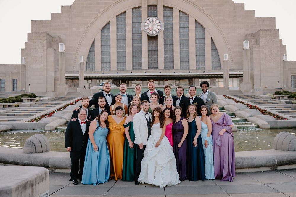 Wedding party poses in colorful gowns before Cincinnati Union Terminal fountain.