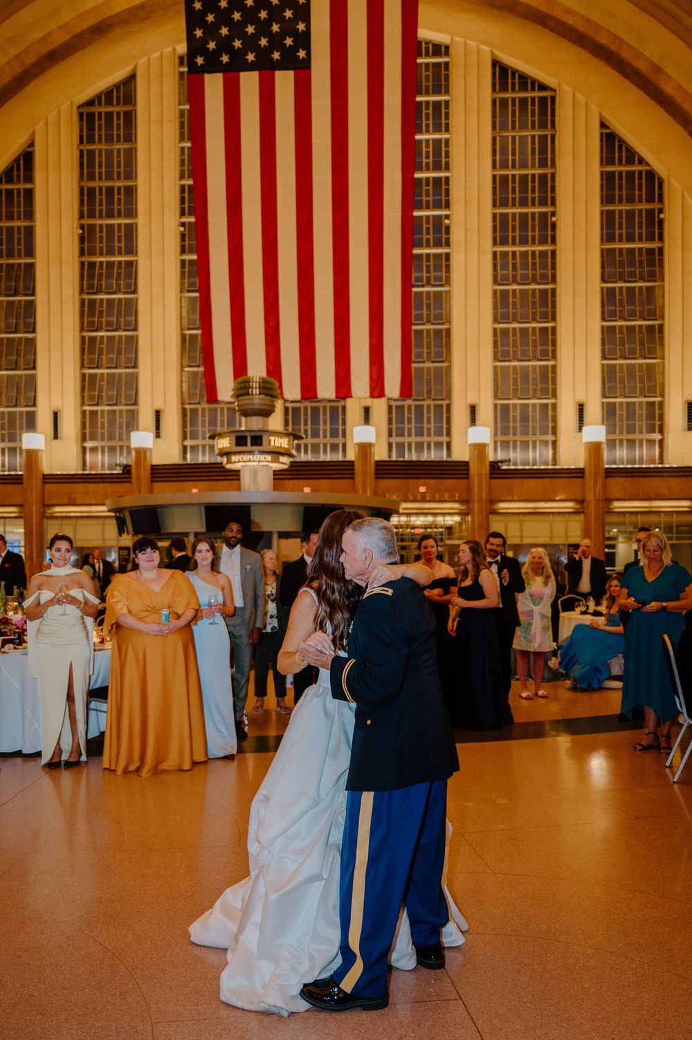 Bride and groom share first dance beneath large American flag in grand Union Terminal ballroom.