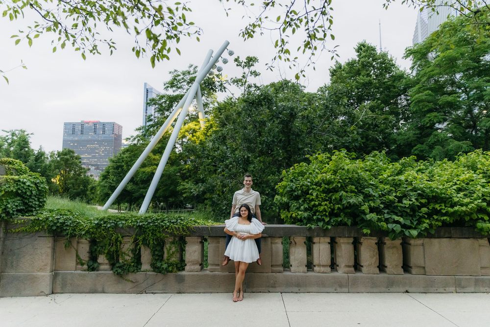 Couple poses in front of lush greenery and city skyline at Millennium Park Chicago engagement photo.