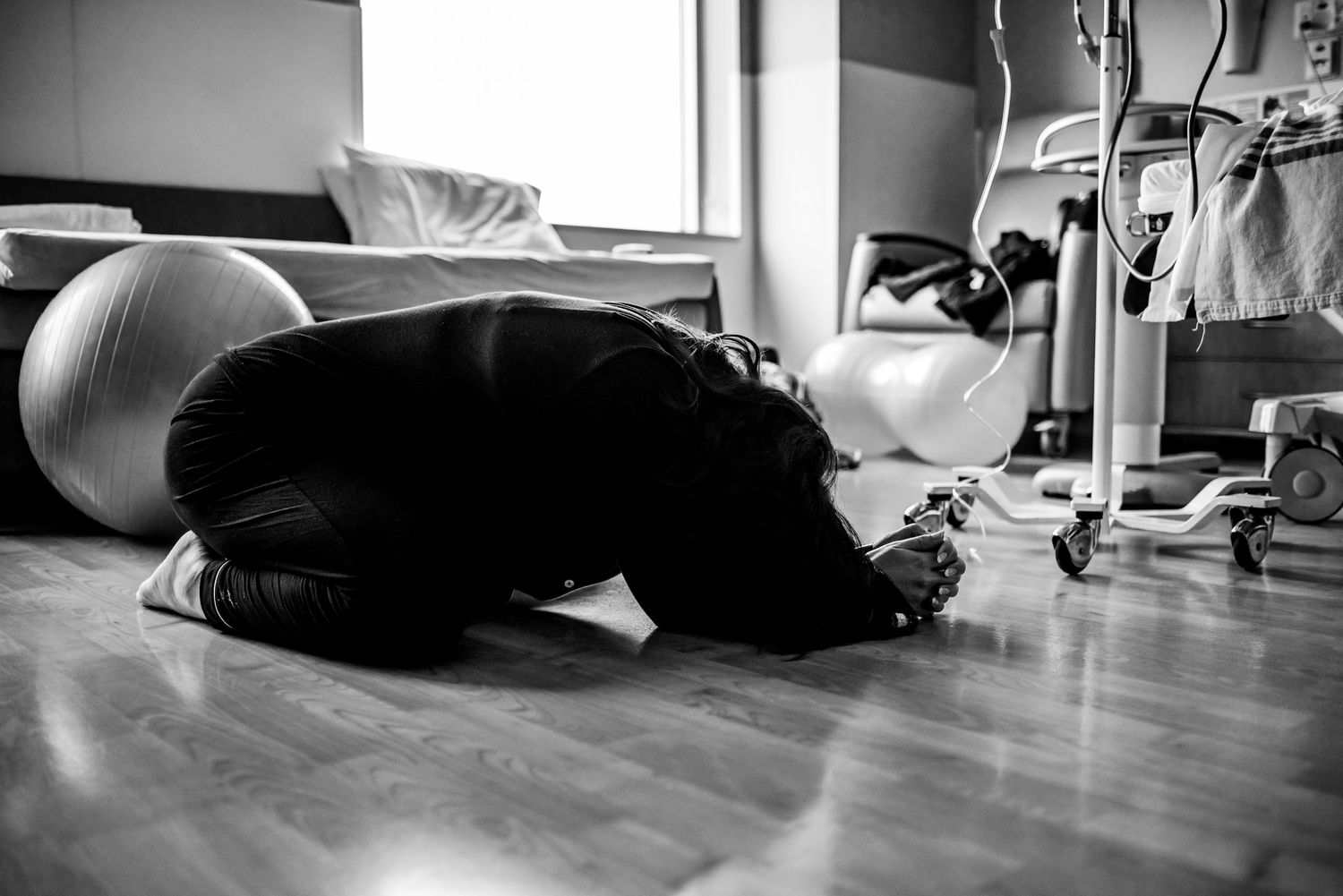 A person lies on the floor in a dark room practicing yoga or meditation in a relaxed pose.