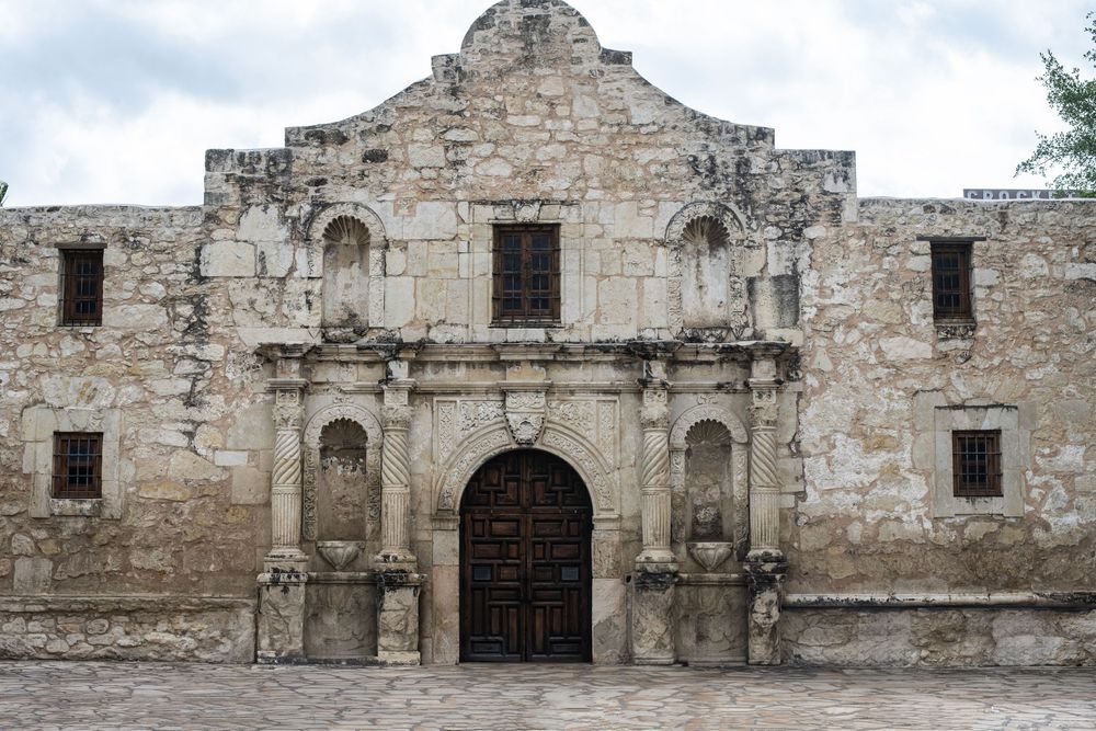 Historic Alamo mission facade in San Antonio, Texas, featuring ornate stone architecture and wooden doors.