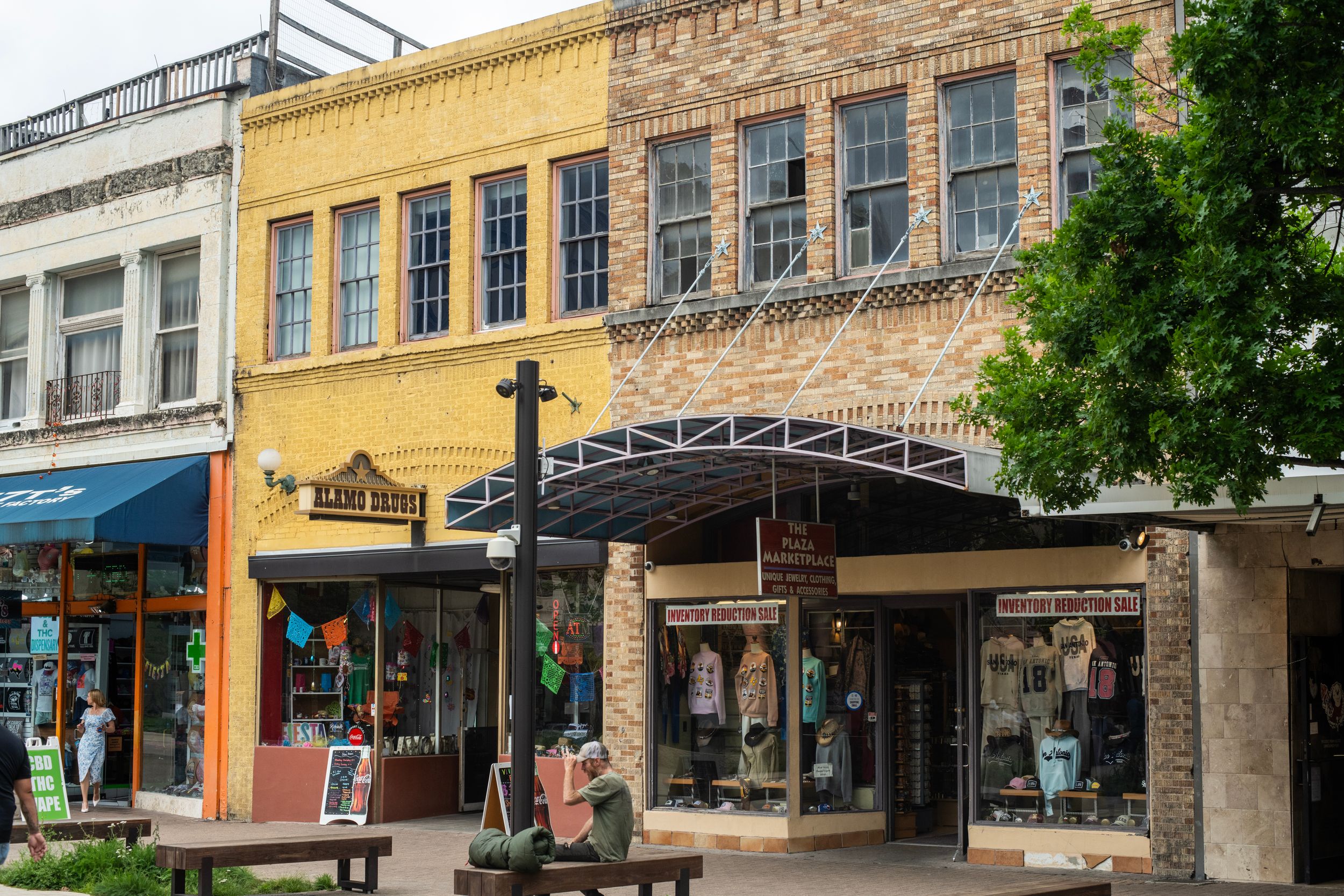 Historic downtown storefronts with yellow brick building, retail shops, and covered walkway on a sunny day.