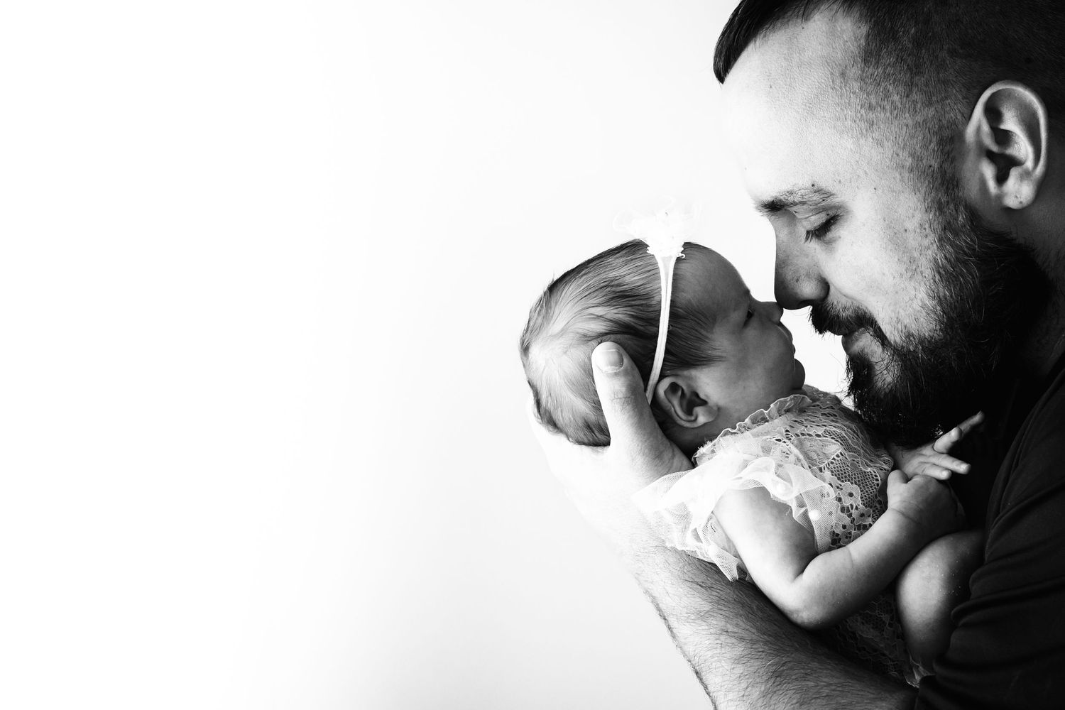 Black and white photo of a father tenderly holding his newborn baby, touching foreheads in an intimate moment.