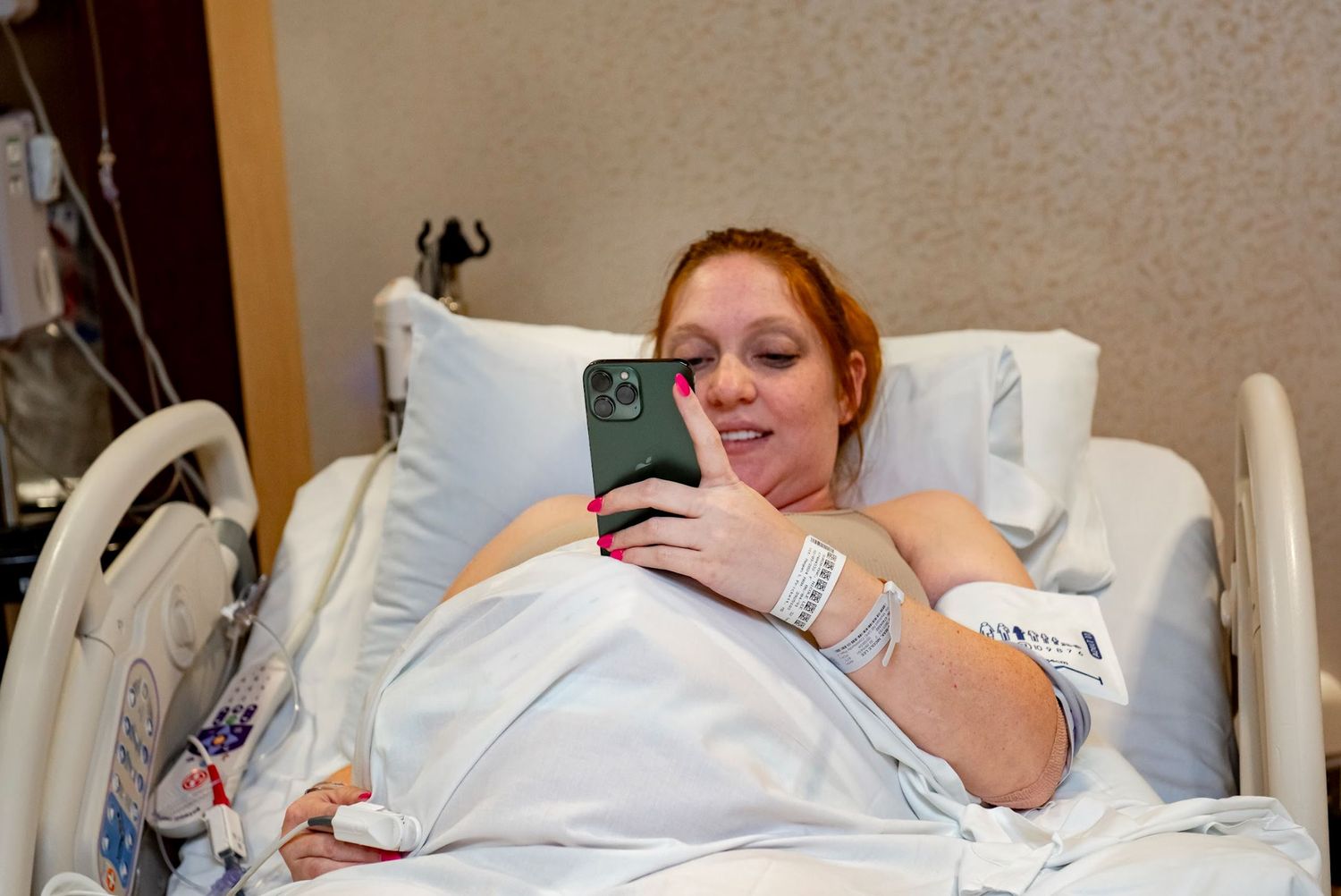 Patient resting in hospital bed checks their phone while in labor.