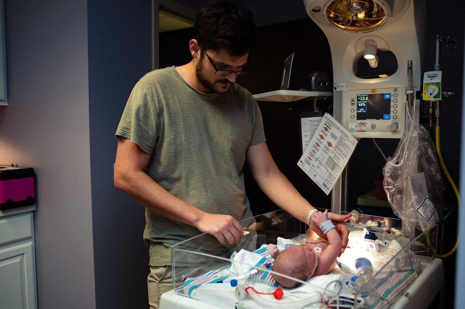 New dad examines newborn baby on medical equipment in hospital setting.