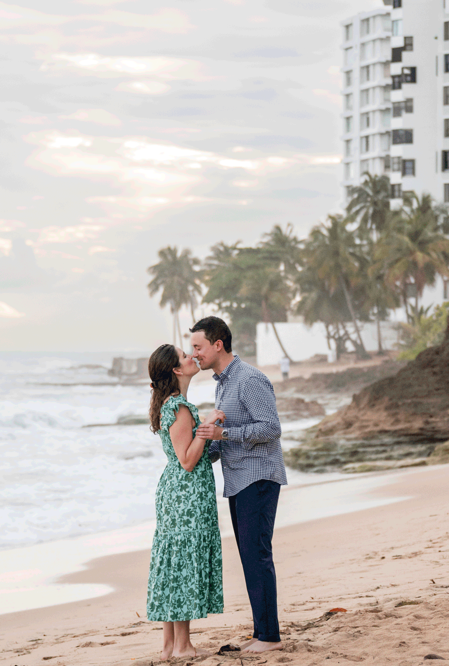 Couple embracing on the beach with palm trees and ocean in the background during a destination engagement session