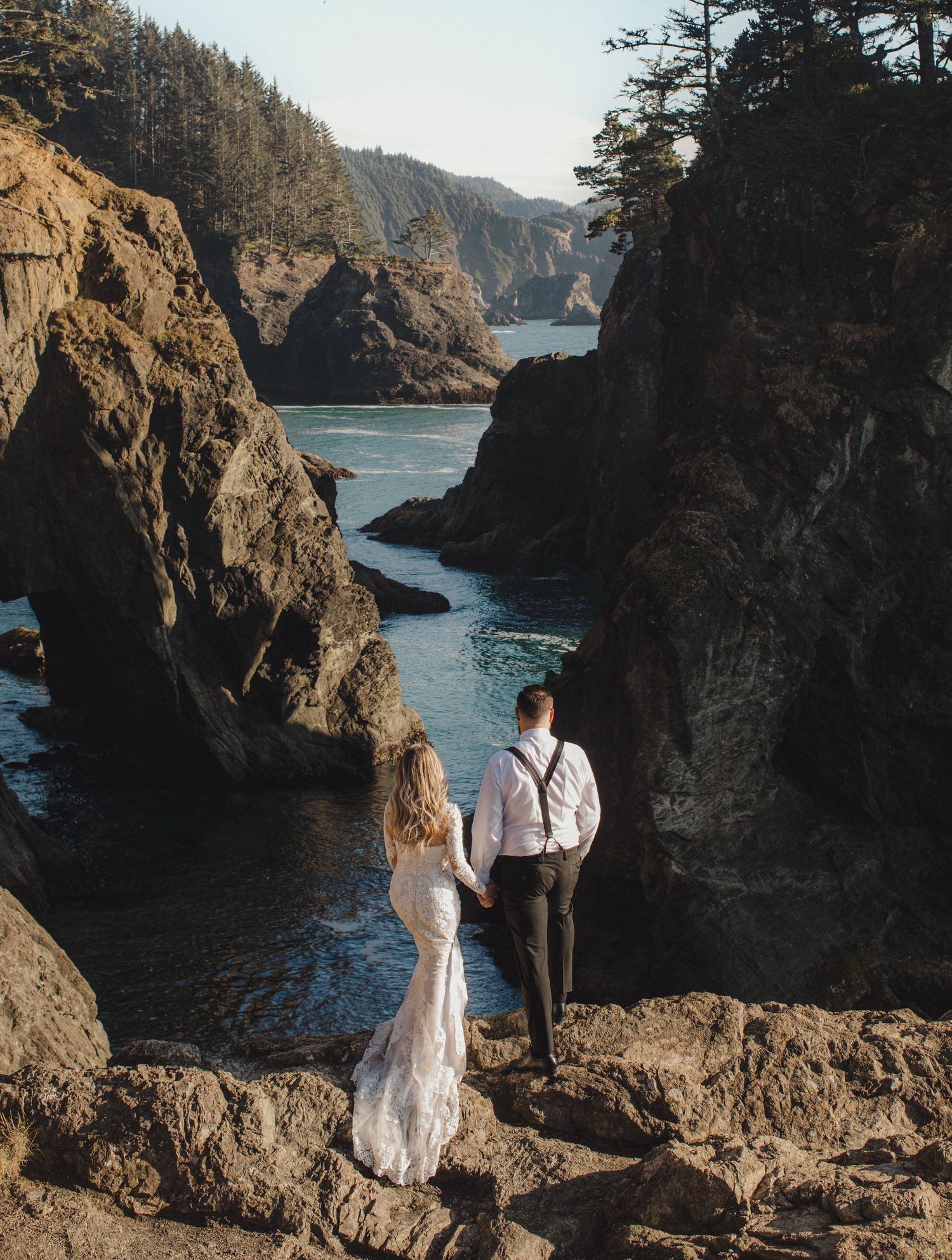 Couple in wedding attire embracing on a misty Oregon coast beach with dramatic sea stacks in the background.