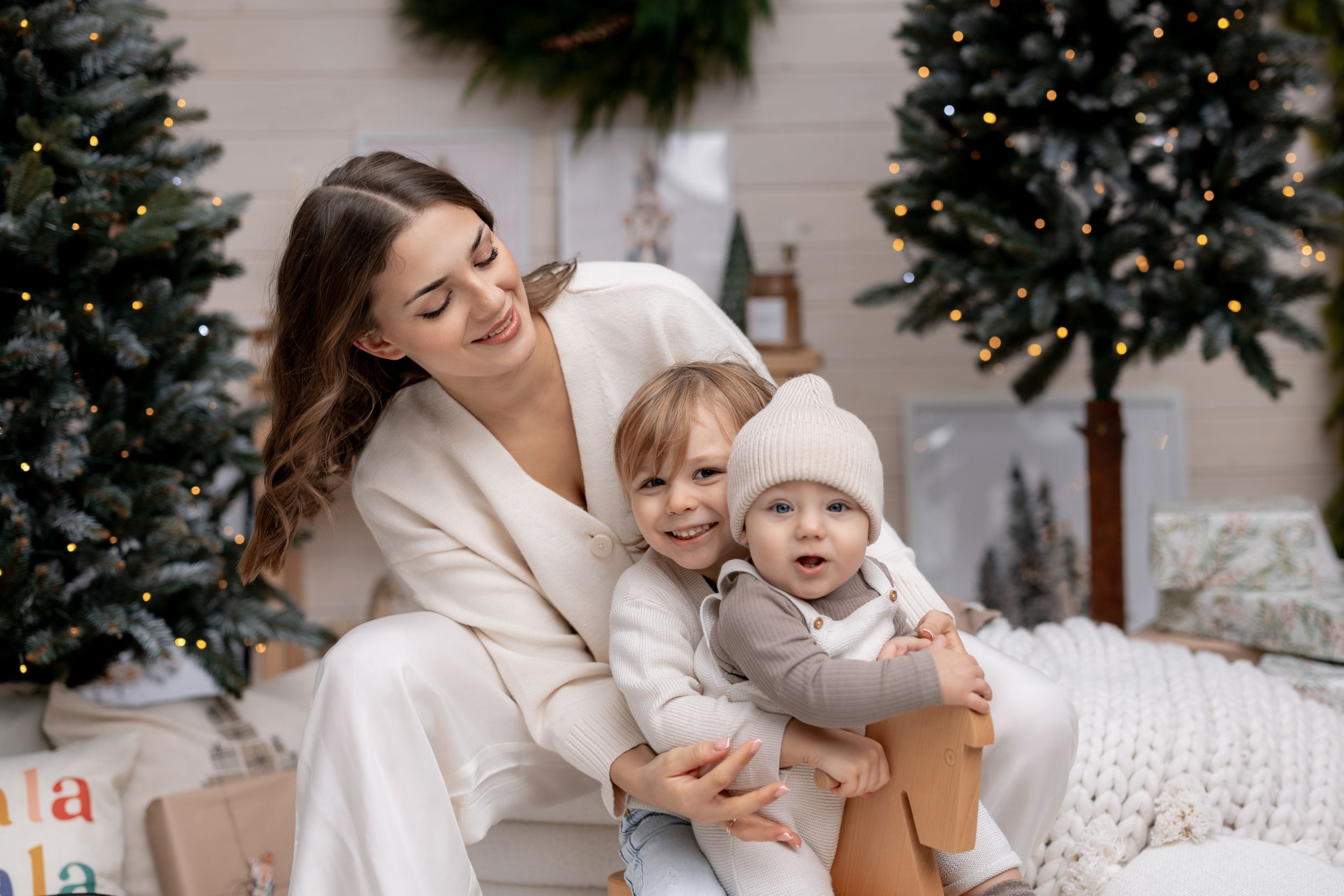 A cozy holiday scene with a family group in white outfits sitting together by decorated Christmas trees.