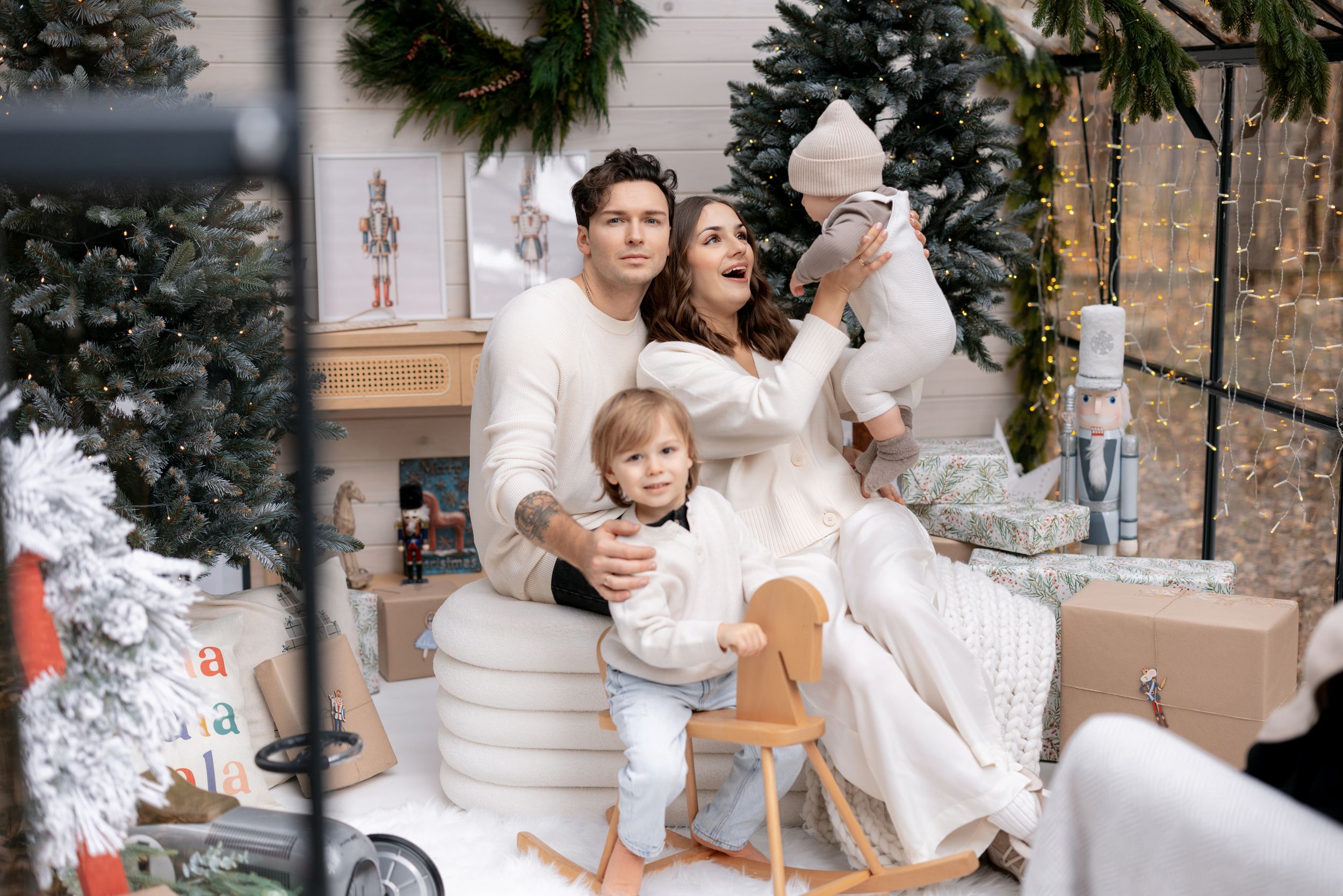 Family dressed in white sharing tender moments during Christmas photoshoot with festive decorations.