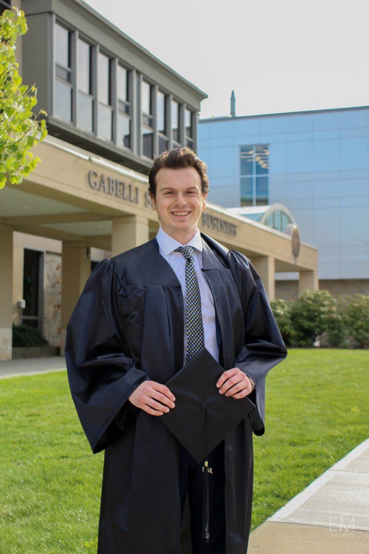 Graduate in academic regalia smiling outside university building on graduation day.